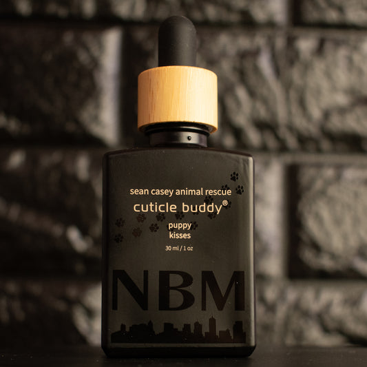 matte Black bottle with wooden dropper labeled 'cuticle buddy' with paw print graphics on a dark background