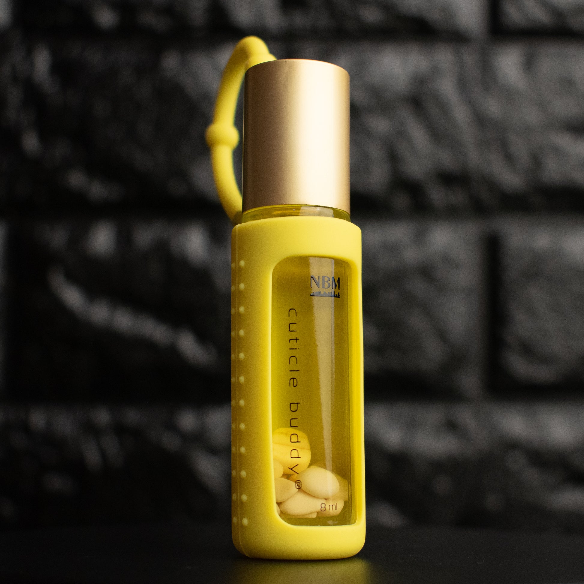 a glass bottle of oil with a gold aluminum cap in a yellow silicone holder on a black brick background. inside the bottle are rose aurora marble stones