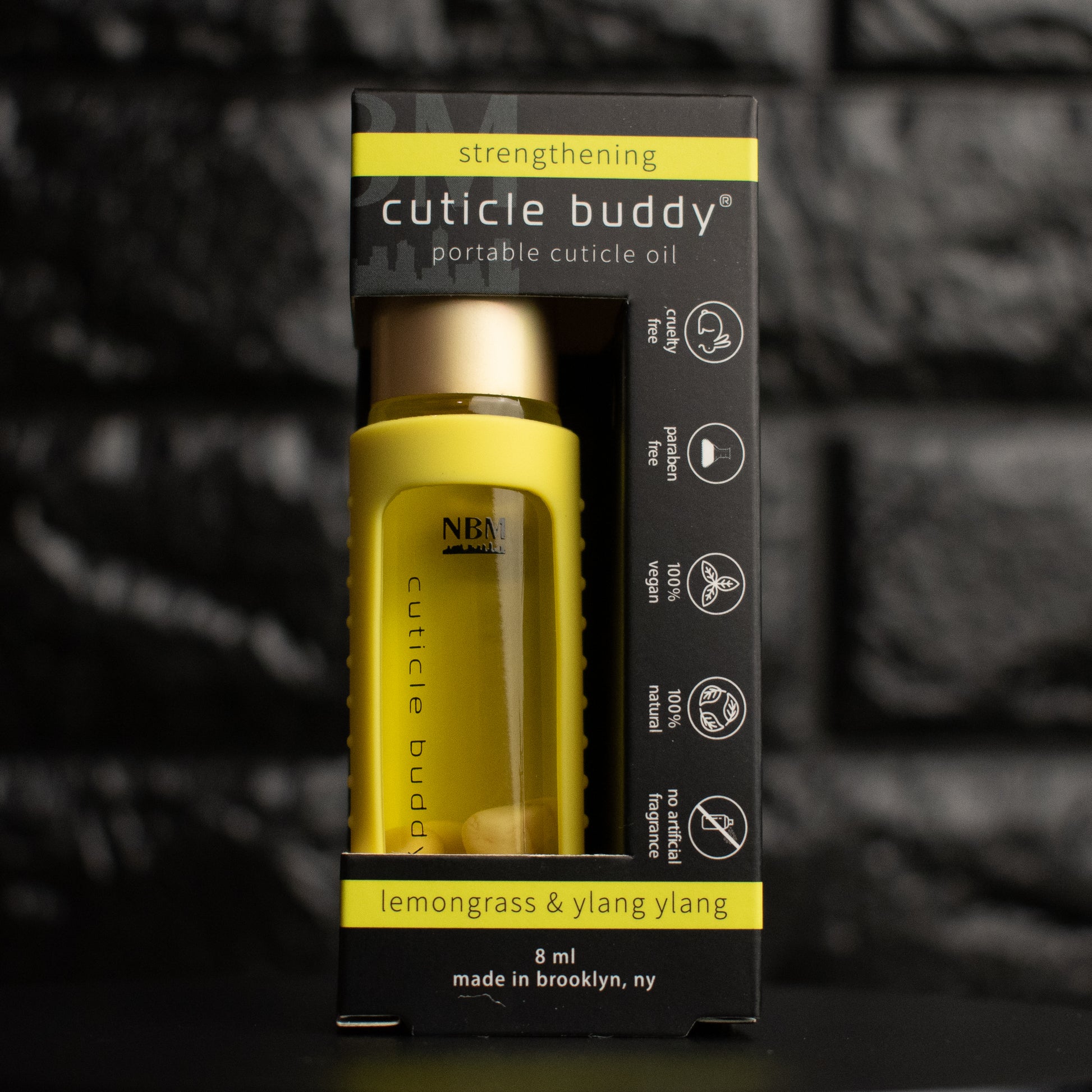 a glass bottle of oil with a gold aluminum cap in a yellow silicone holder on a black brick background. inside the bottle are rose aurora marble stones. in its packaging box