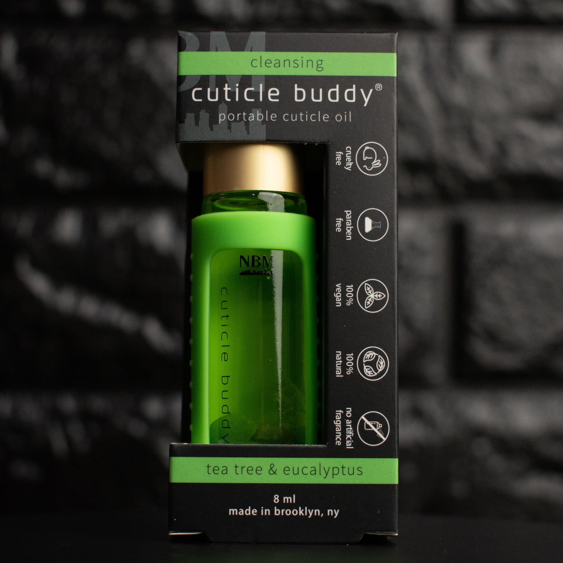 a glass bottle of oil with a gold aluminum cap in a green silicone holder on a black brick background. inside the bottle are green aventurine stones. in its packaging box.