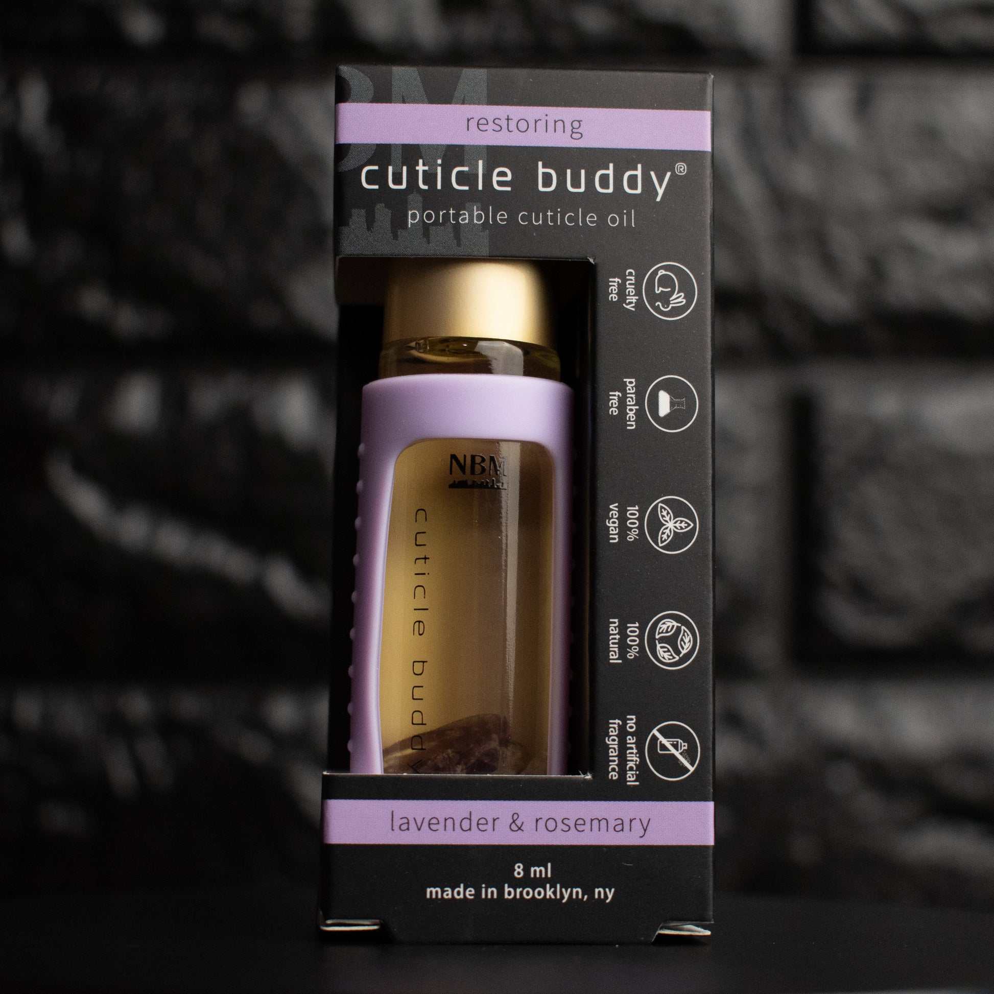 a glass bottle of oil with a gold aluminum cap in a purple silicone holder on a black brick background. inside the bottle are purple amethyst stones. in its packaging box