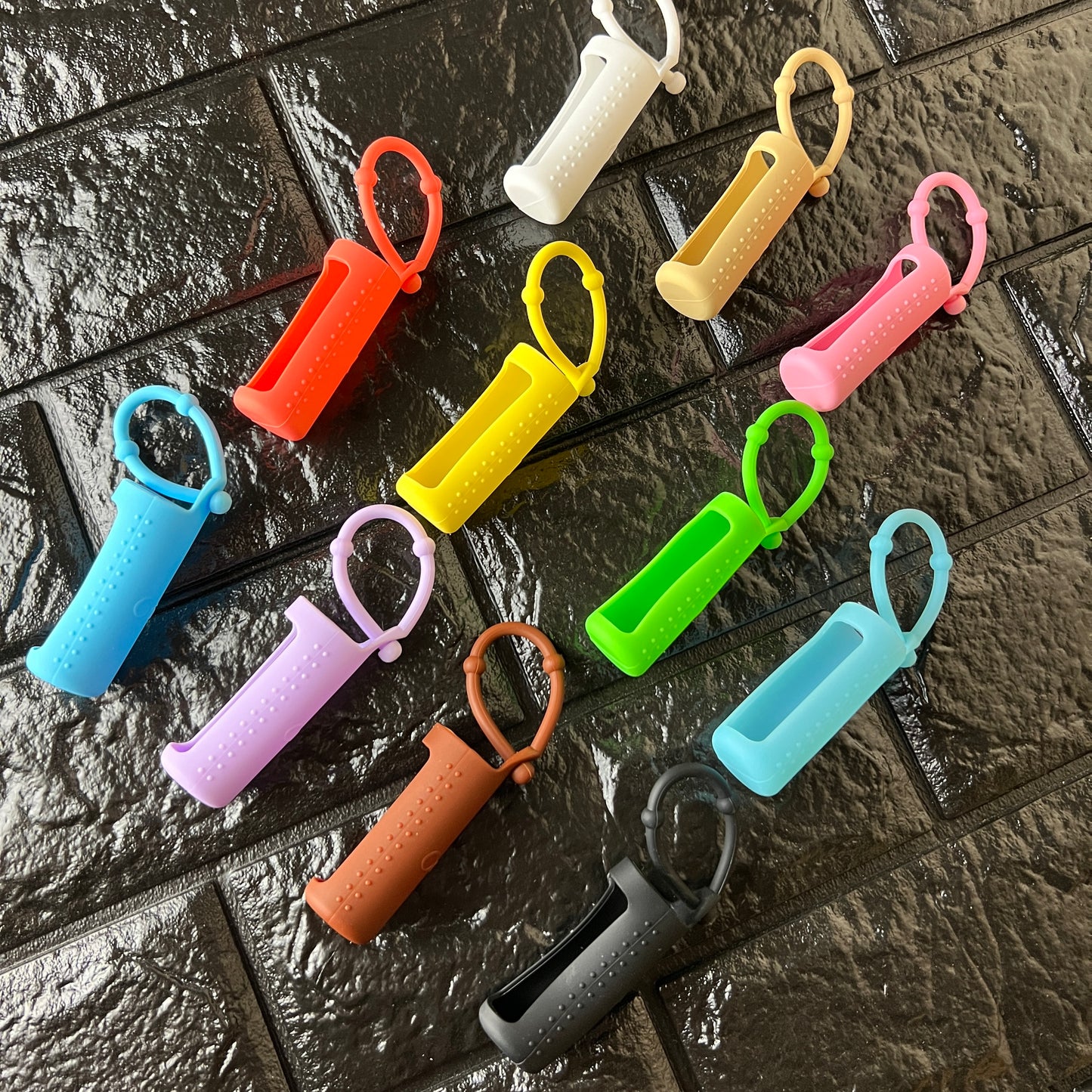 A collection of silicone cuticle buddy holders in various solid colors, including white, beige, pink, orange, yellow, green, jelly blue, opaque blue, light purple, brown and black