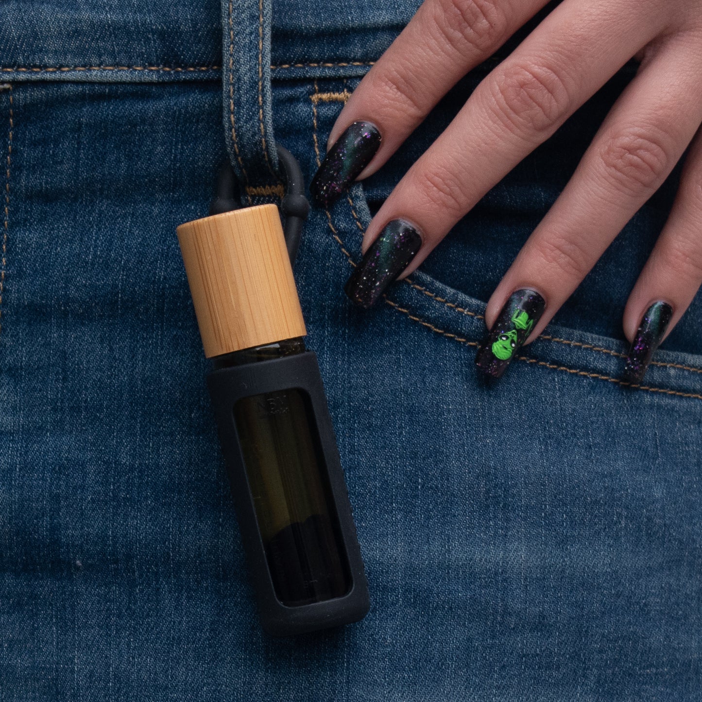 a bottle of cuticle buddy in a black silicone holder hanging off the belt loop of a pair of jeans