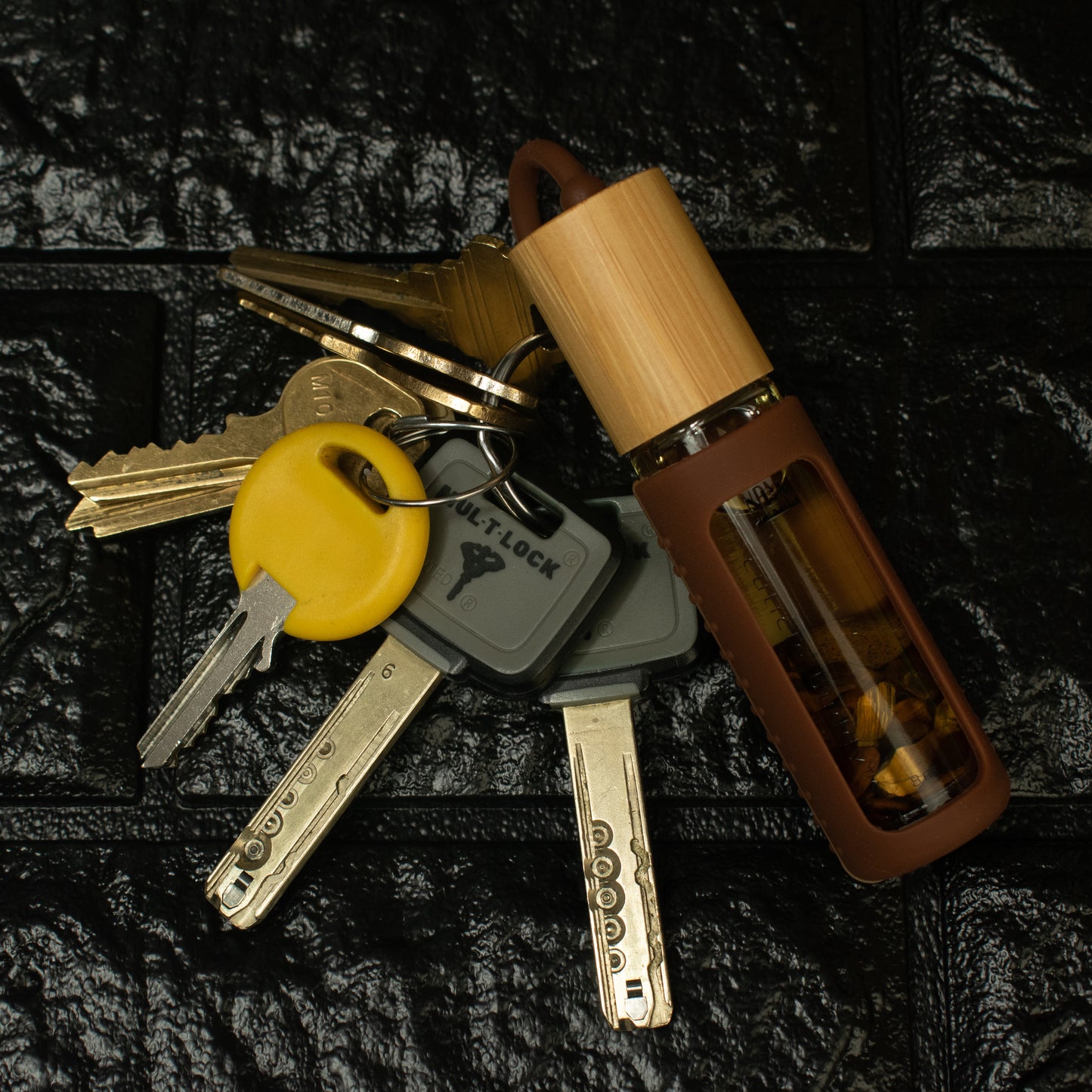 a bottle of cuticle oil in a brown silicone holder attached to a set of keys on a black brick background