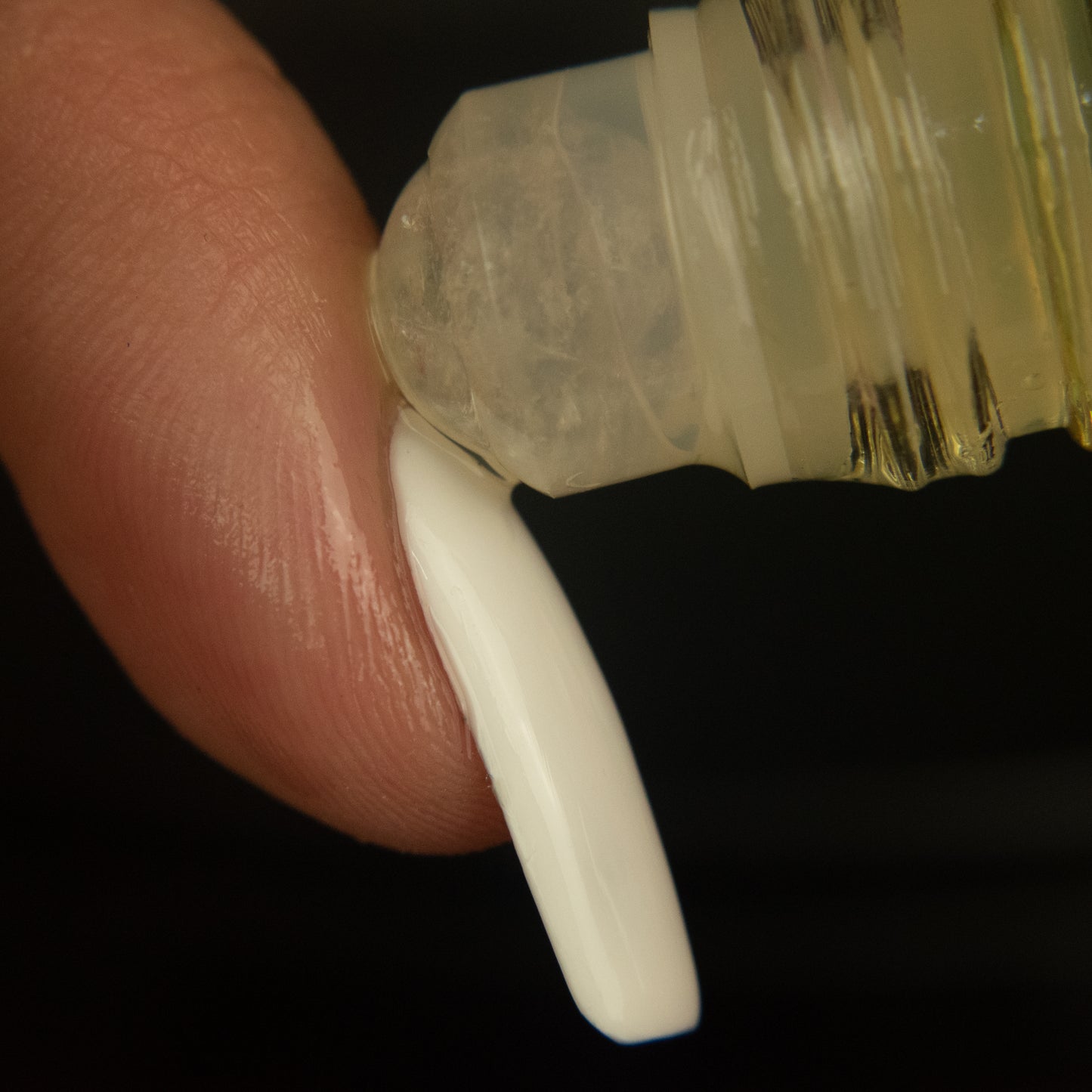 quartz rollerball of cuticle oil being applied onto the cuticle of a finger with a long white nail