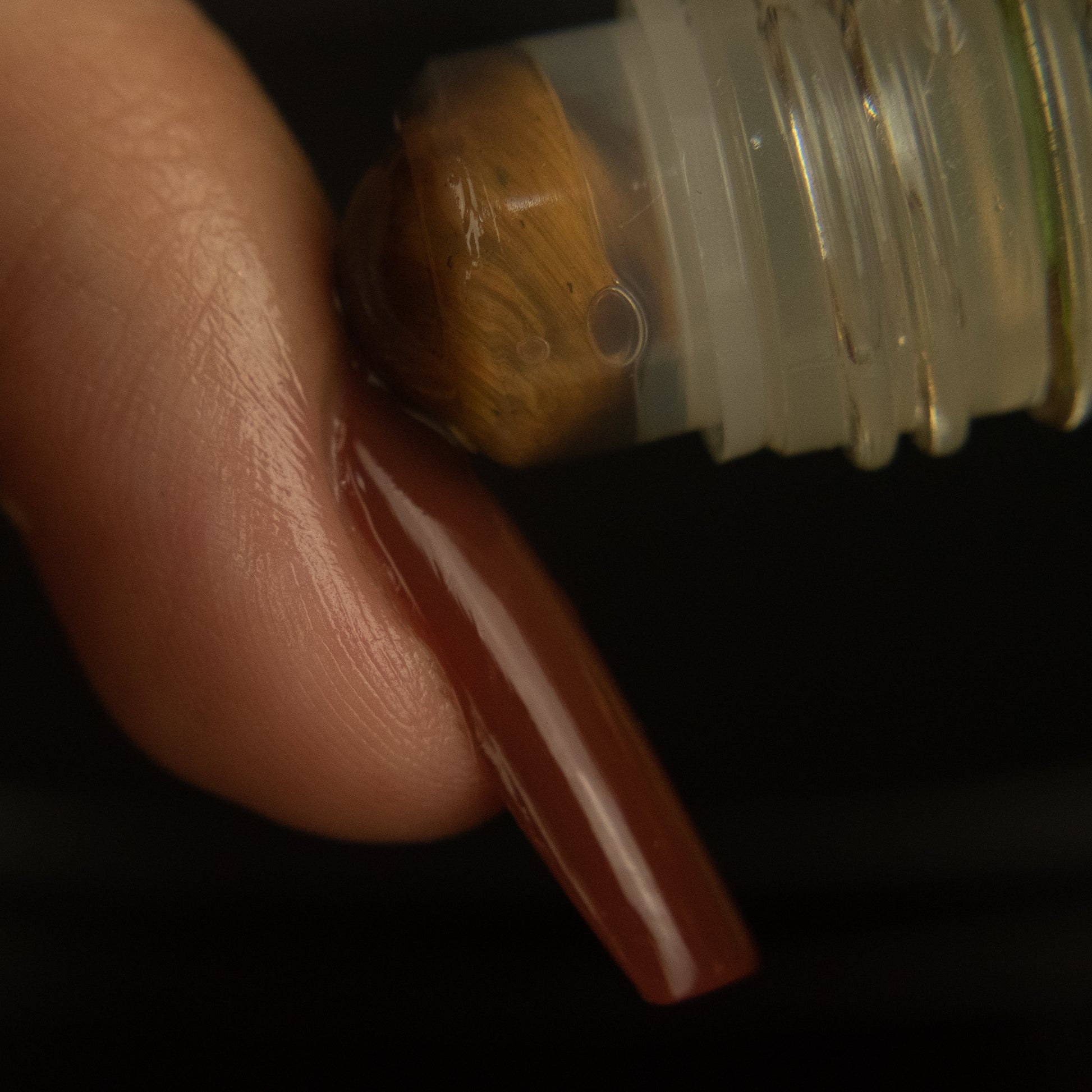 brown tigers eye rollerball being rolled onto the cuticle of a long brown nail