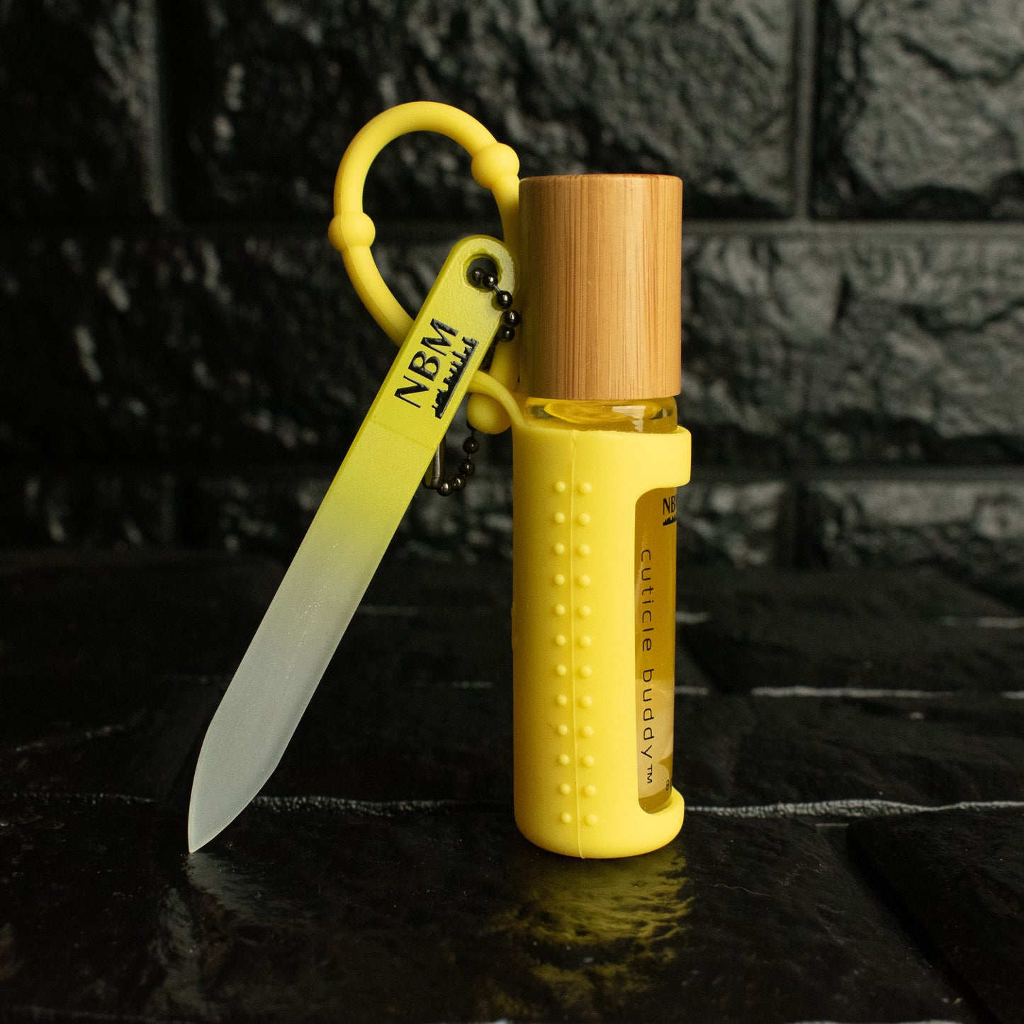 nbm yellow portable glass nail file hanging off a cuticle buddy in a yellow silicone holder