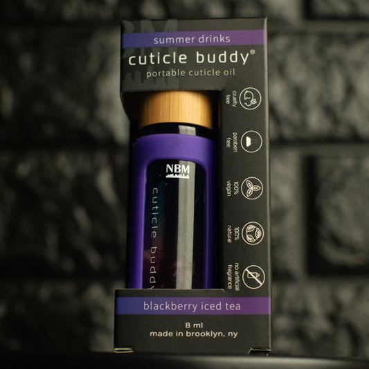 Purple rollerball bottle in a purple silicone cover with gold aluminum cap labeled cuticle buddy blackberry iced tea in it's box on a dark textured background