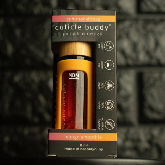 orange rollerball bottle in an orange silicone cover with gold aluminum cap labeled cuticle buddy mango smoothie in it's box on a dark textured background