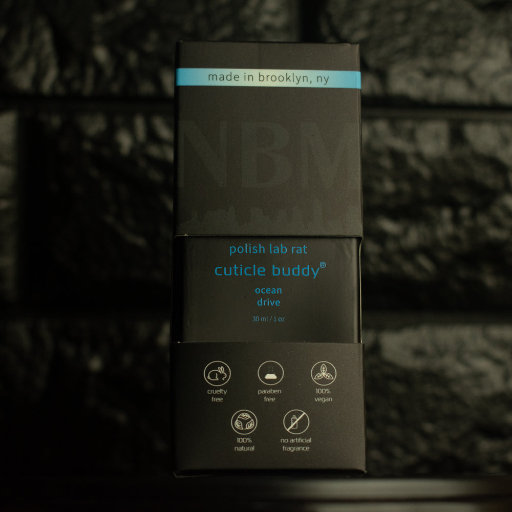 matte Black bottle with wooden dropper labeled polish lab rat cuticle buddy ocean drive 30ml/1oz in its packaging box, on  a dark background