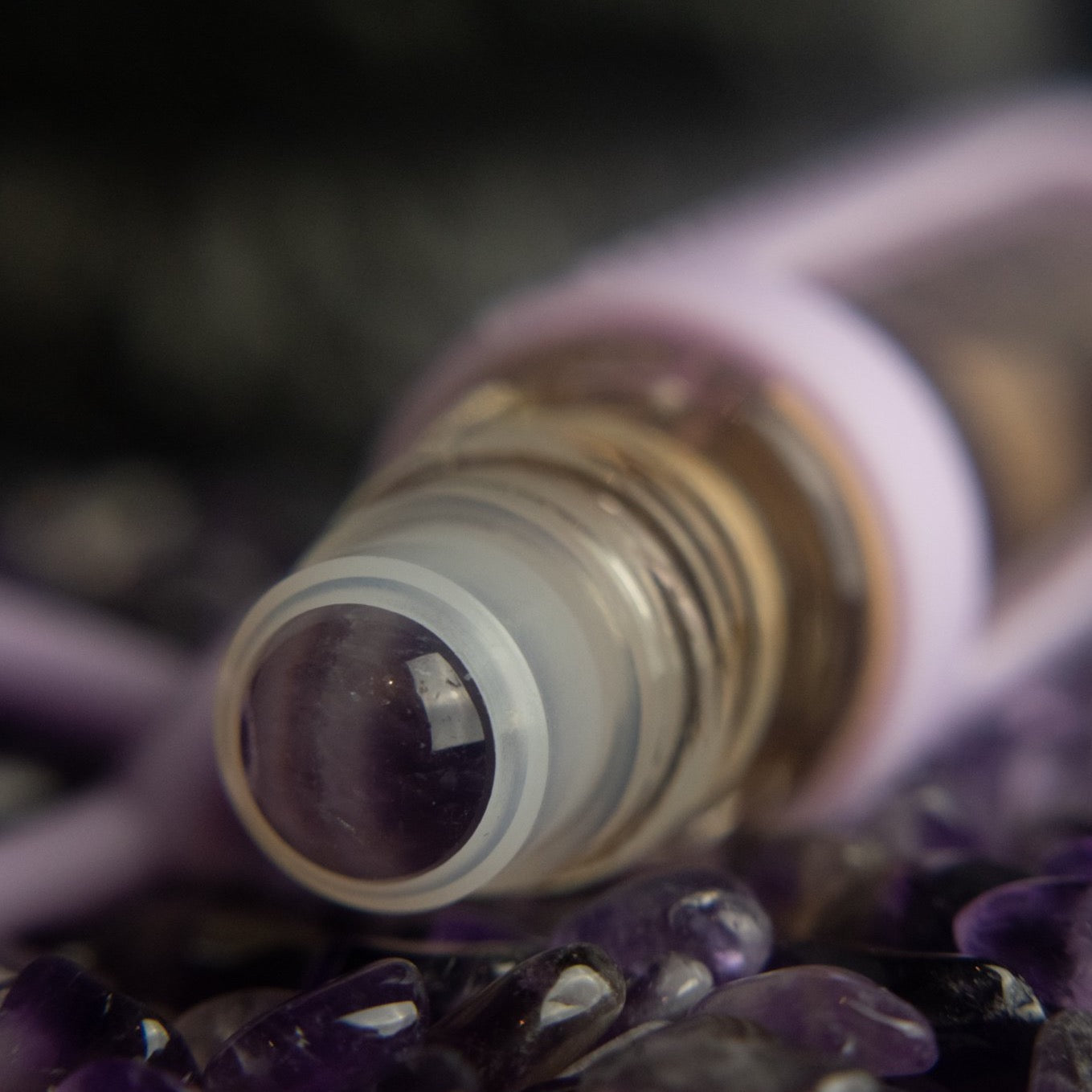 cuticle buddy™ restoring portable cuticle oil amethyst rollerball closeup in a bed of amethyst stones