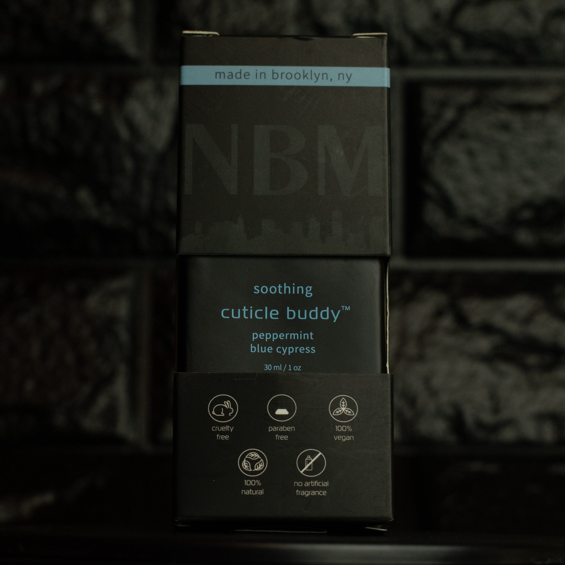 matte Black bottle with wooden dropper labeled soothing cuticle buddy peppermint blue cypress 30ml/1oz in its packaging box  on  a dark background