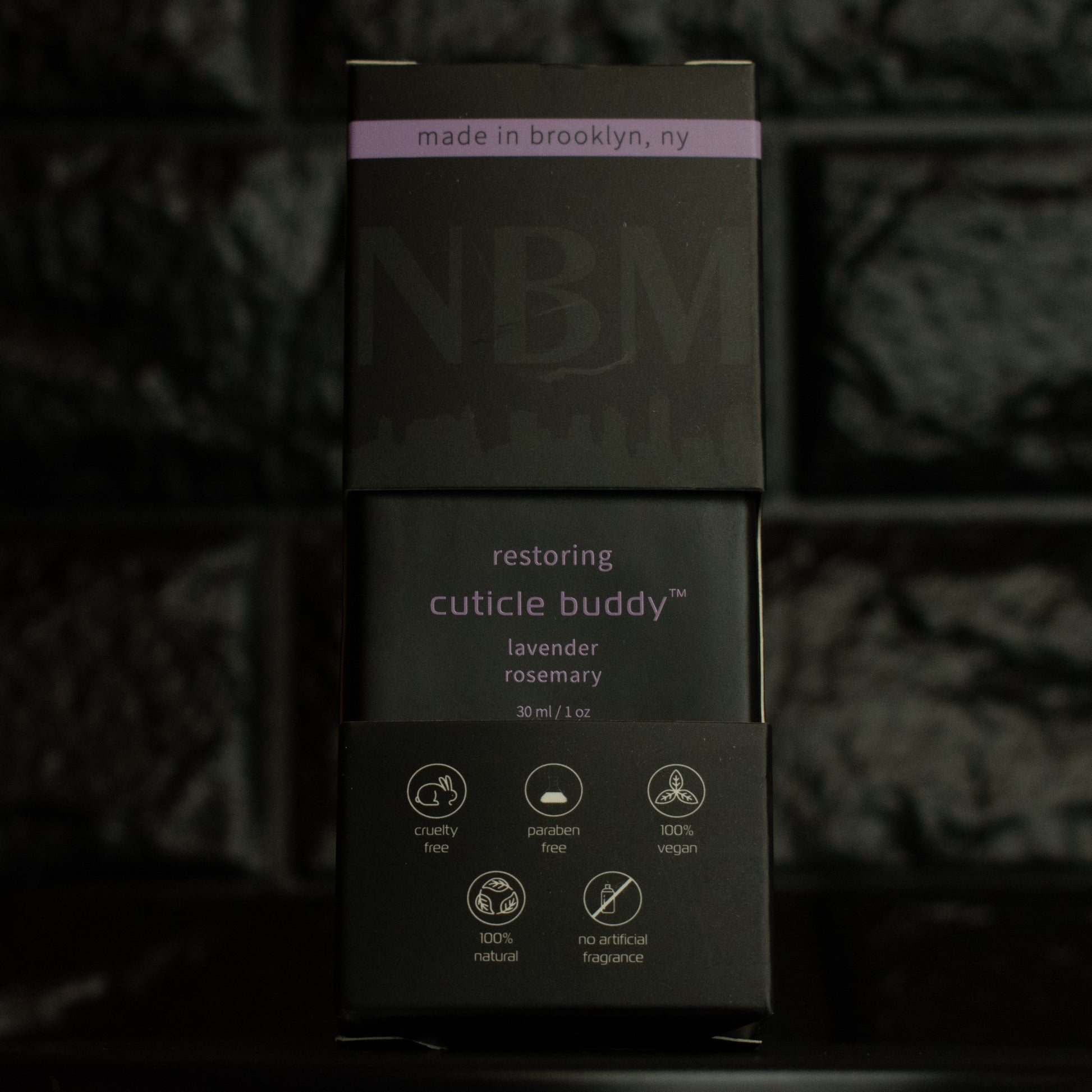 matte Black bottle with wooden dropper labeled restoring cuticle buddy lavender rosemary 30ml/1oz in its packaging box on  a dark background
