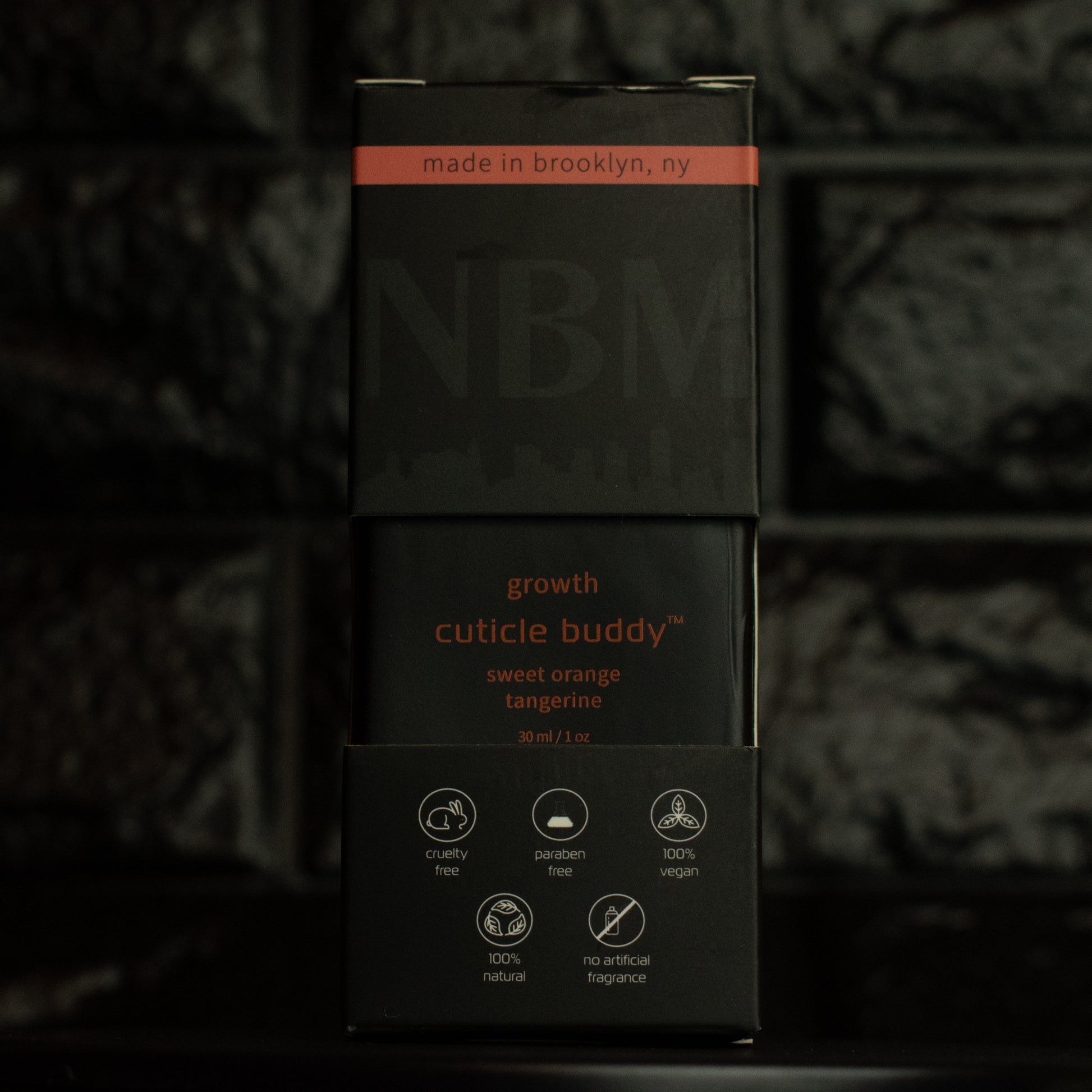 matte Black bottle with wooden dropper labeled growth cuticle buddy sweet orange tangerine 30ml/1oz in its packaging box, on  a dark background