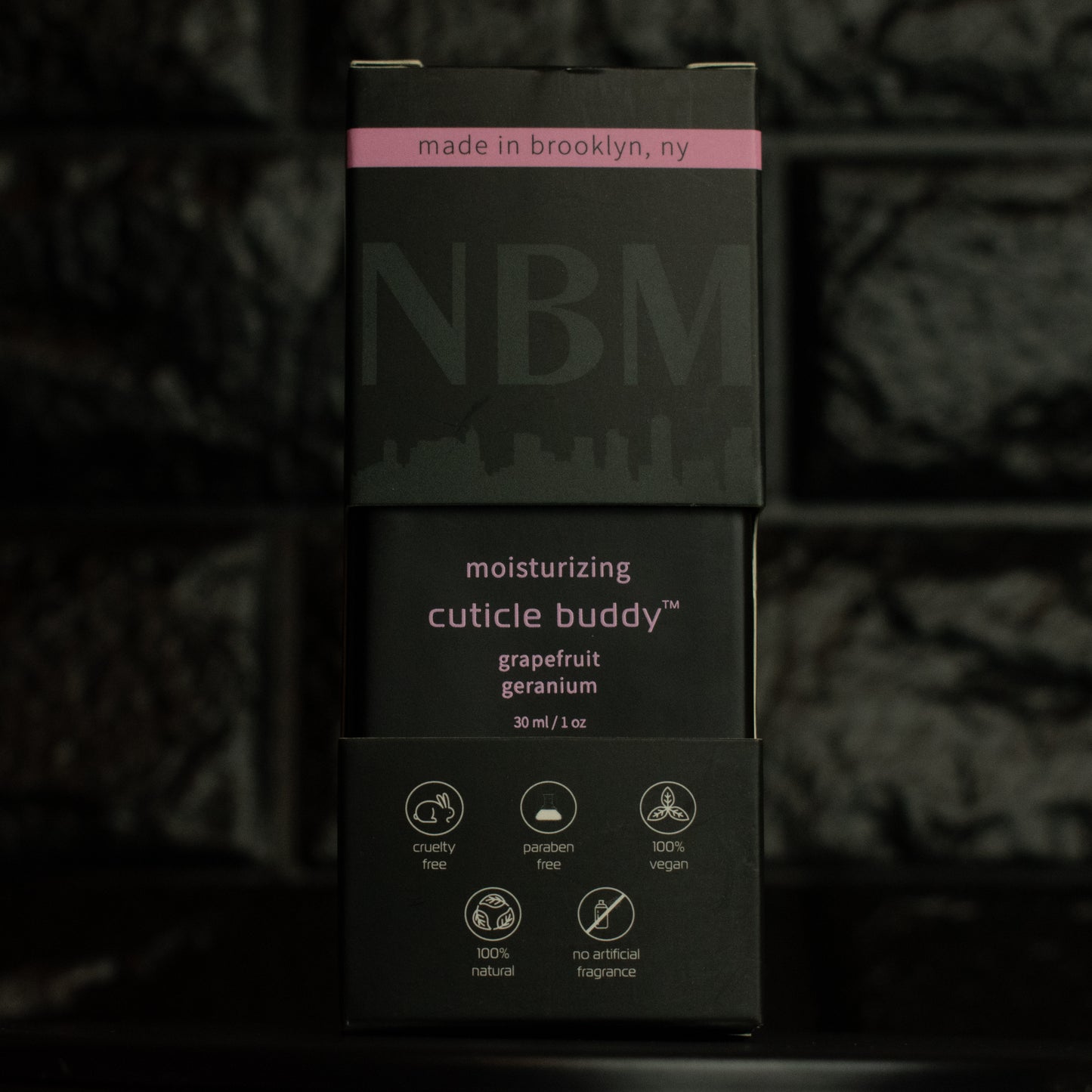 matte Black bottle with wooden dropper labeled moisturizing cuticle buddy grapefruit geranium 30ml/1oz in its packaging box on  a dark background
