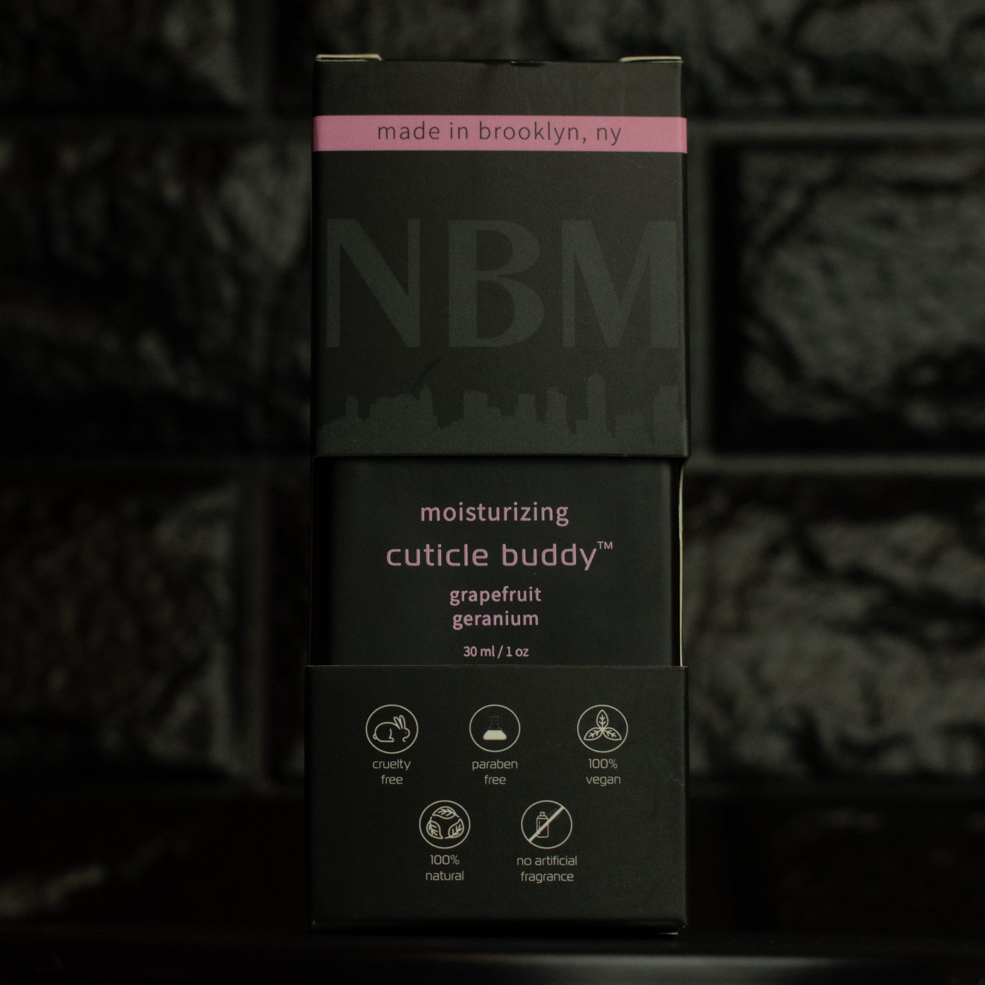 matte Black bottle with wooden dropper labeled moisturizing cuticle buddy grapefruit geranium 30ml/1oz in its packaging box on  a dark background