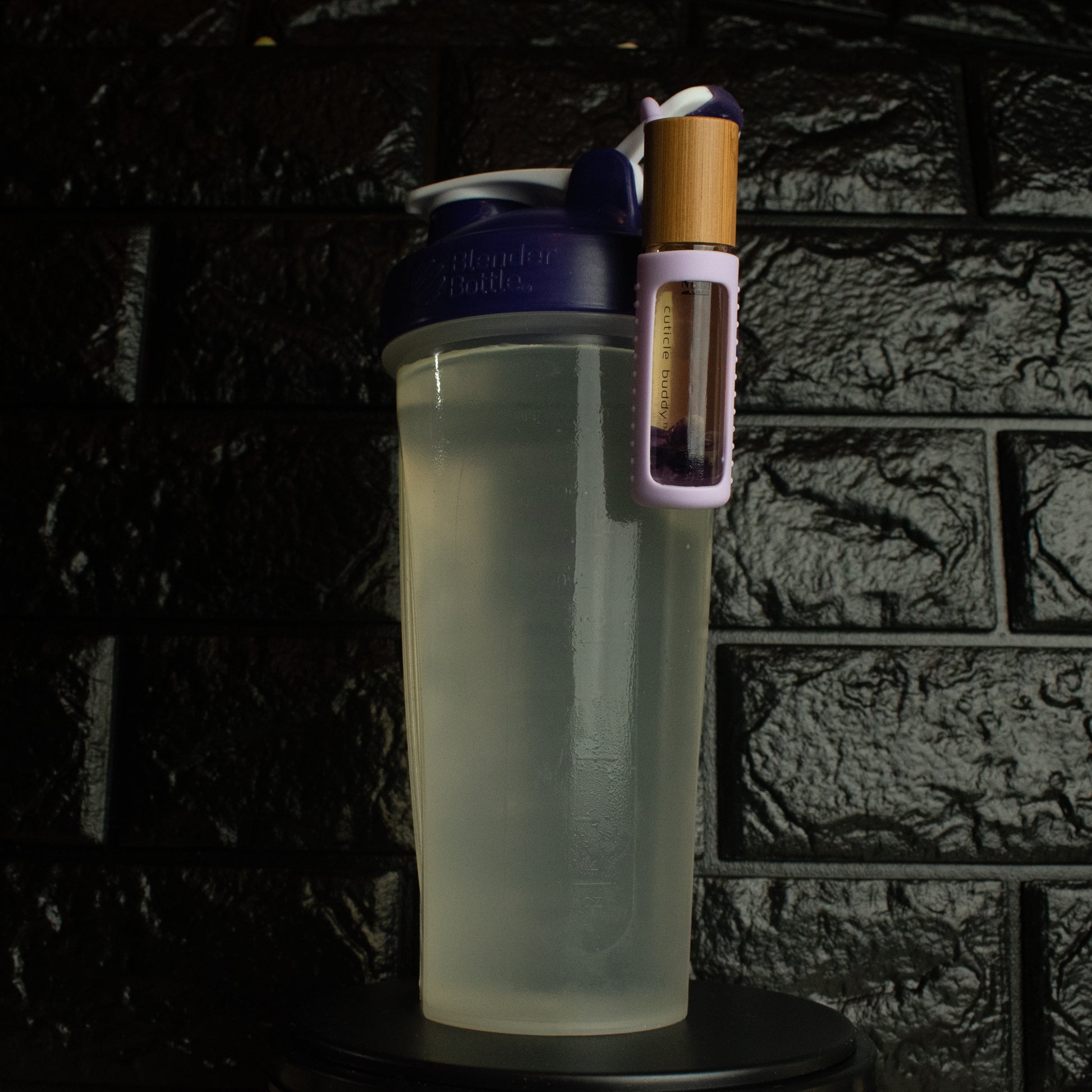 a bottle of cuticle oil in a purple silicone holder hanging off a portable plastic water bottle