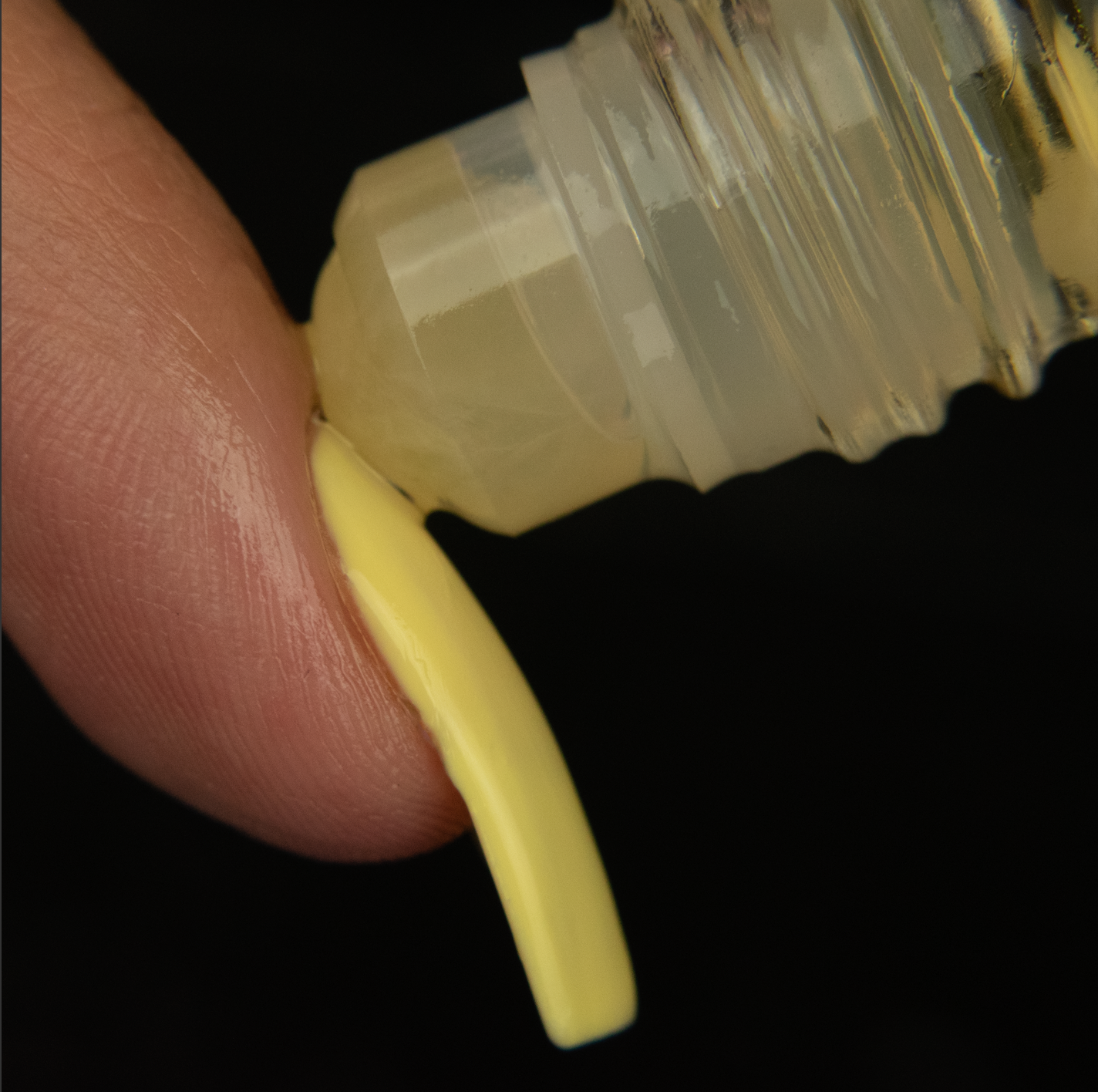 a yellow jade rollerball being applied to the cuticle of a finger with a long yellow nail