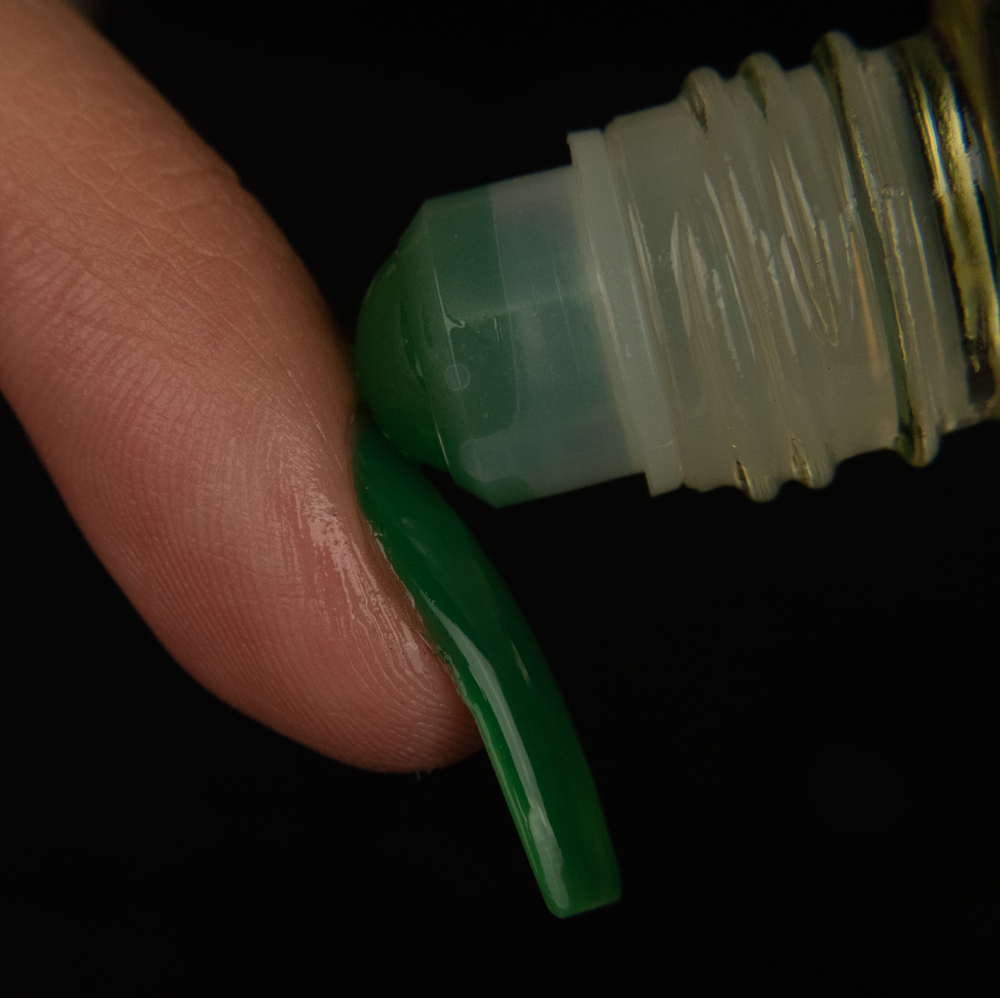close up of a green aventurine  rollerball being rolled onto the cuticle of a finger with a long green nail