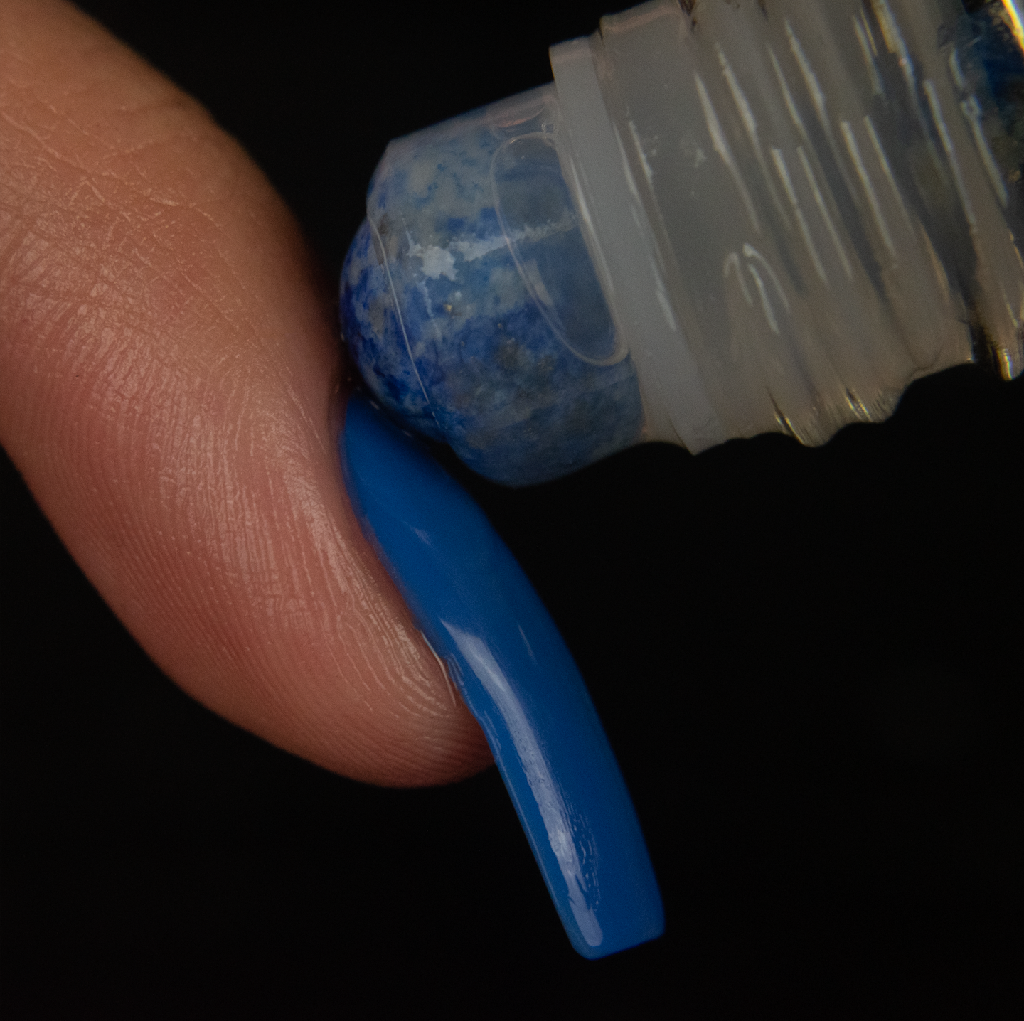 close up of a blue sodalite rollerball being rolled onto the cuticle of a finger with a long blue nail