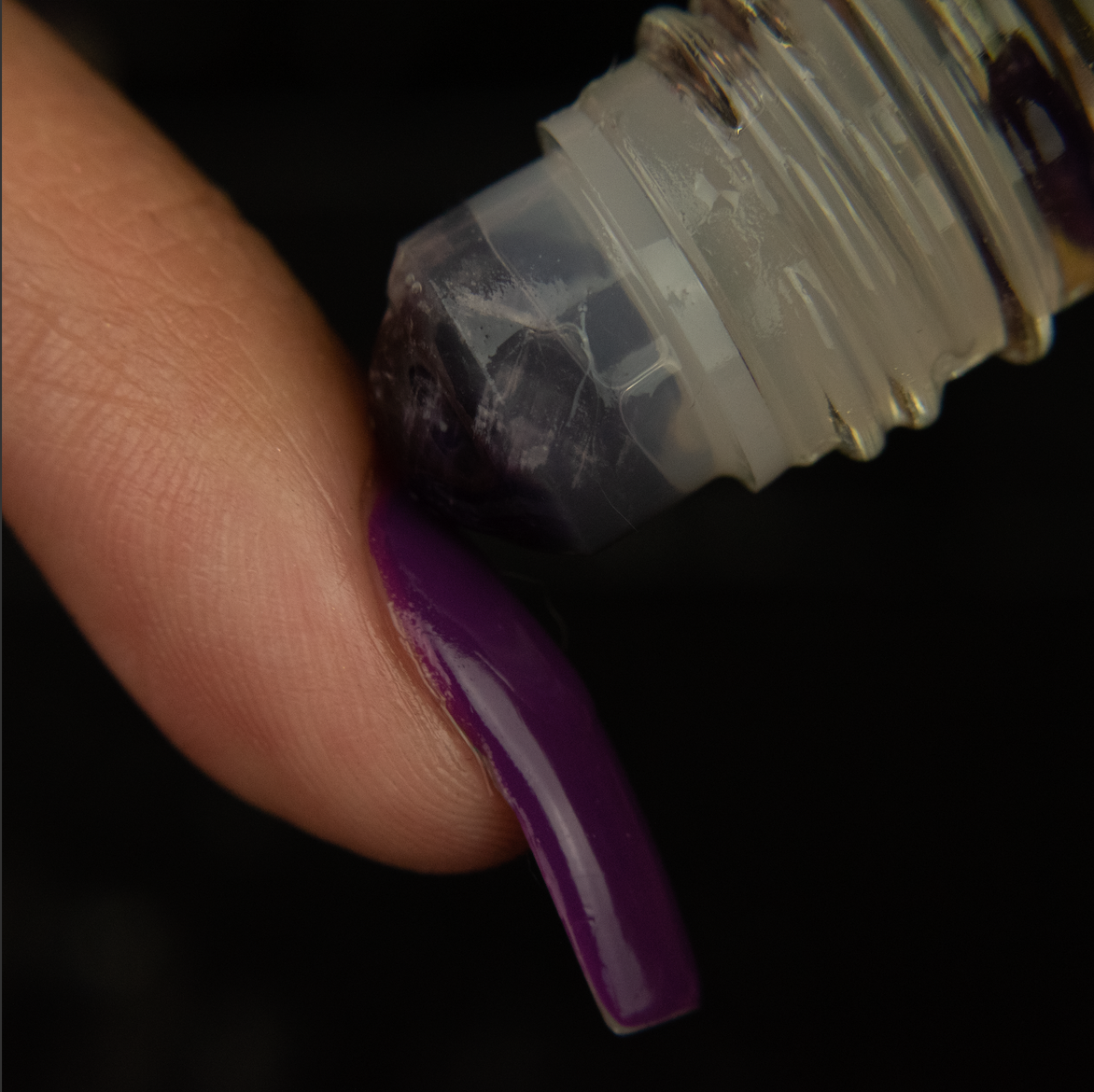 an amethyst rollerball rolling onto the cuticle of a finger with a long purple painted nail