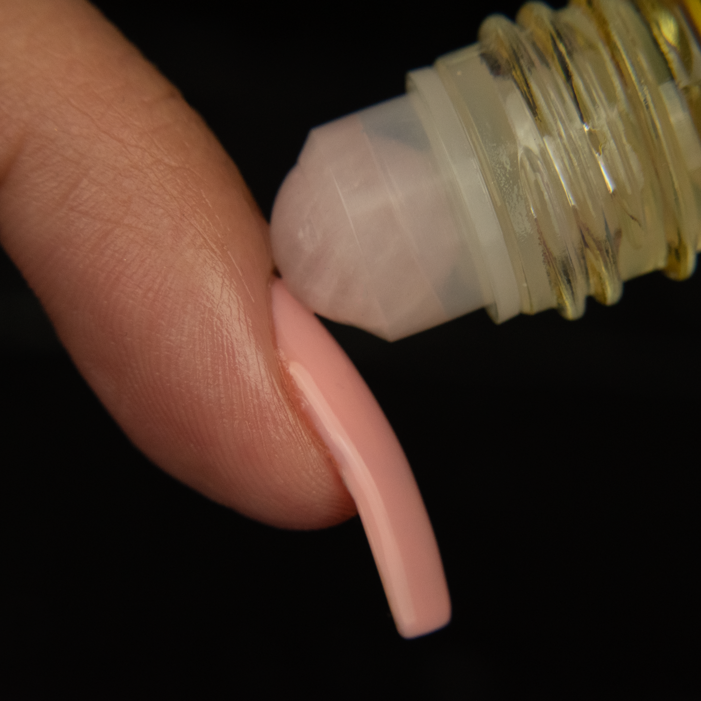 close up of a rose quartz rollerball being rolled onto the cuticle of a finger with a long pink nail