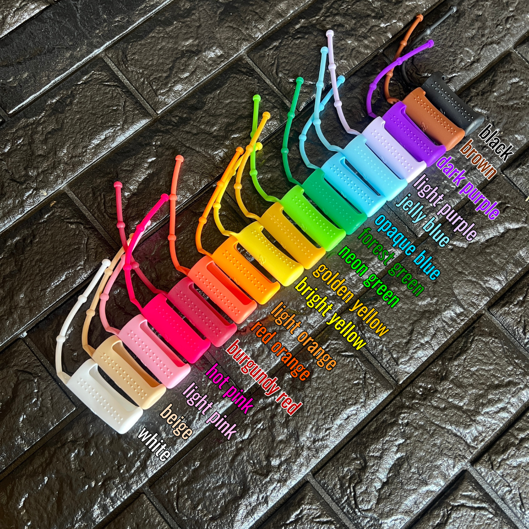 assortment of different colored silicone holders on a black brick background, labeled from left to right: white, beige, light pink, hot pink, burgundy red, red orange, light orange, bright yellow, golden yellow, neon green, forest green, opaque blue, jelly blue, light purple, dark purple, brown, black
