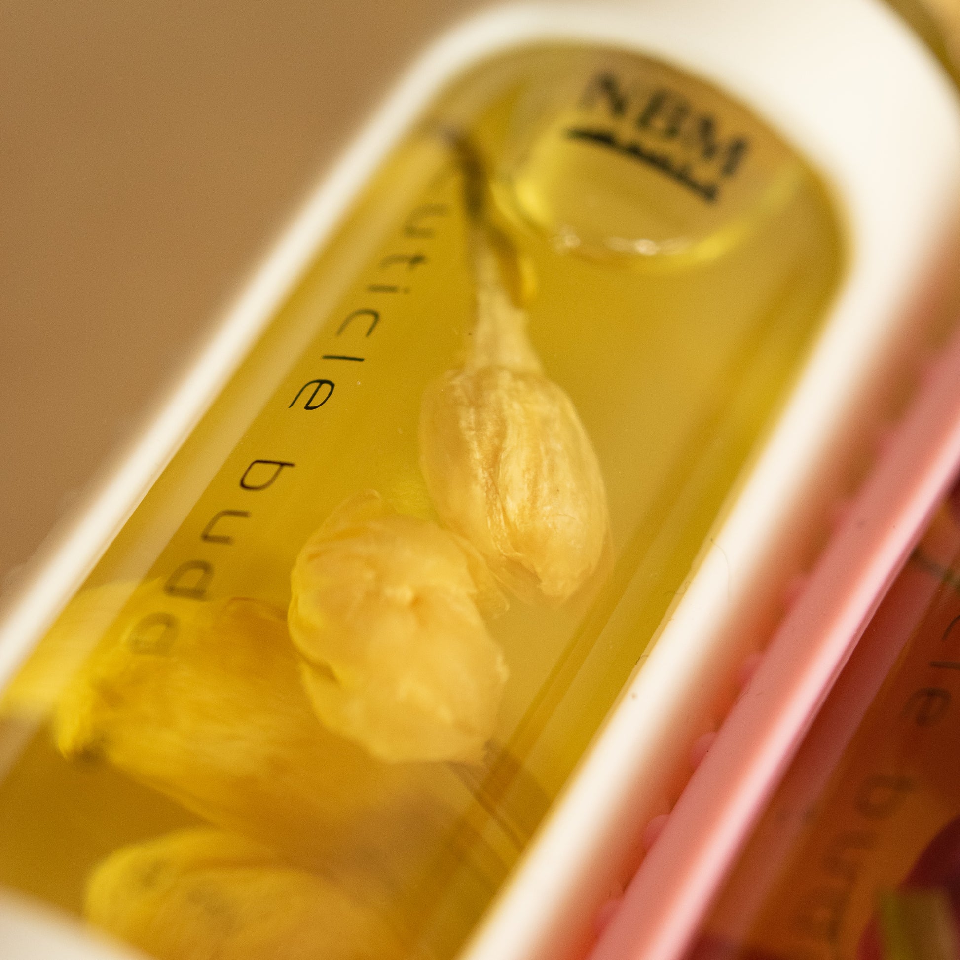 close up of a bottle of cuticle oil with a white silicone holder and jasmine buds inside