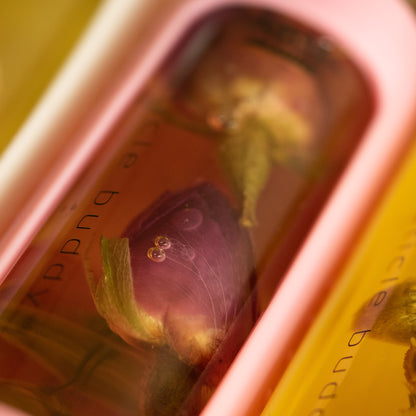 close up of a bottle of cuticle oil in a pink silicone holder and rose buds inside