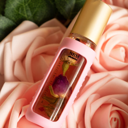 a bottle of cuticle oil with a gold cap in a pink silicone holder and rose buds inside on a bed of pink roses