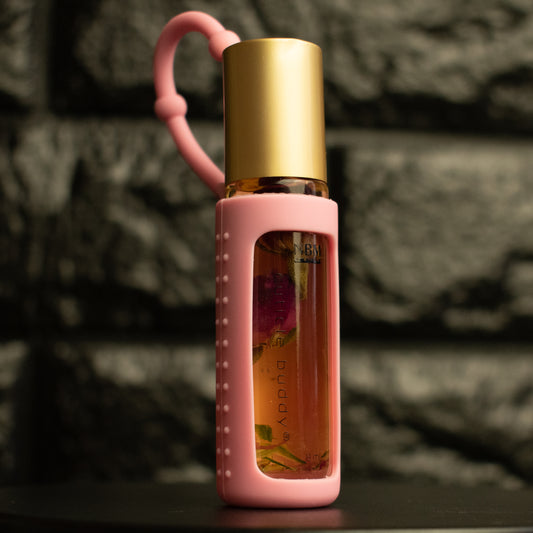 a bottle of cuticle oil with a gold cap in a pink silicone holder and rose buds inside