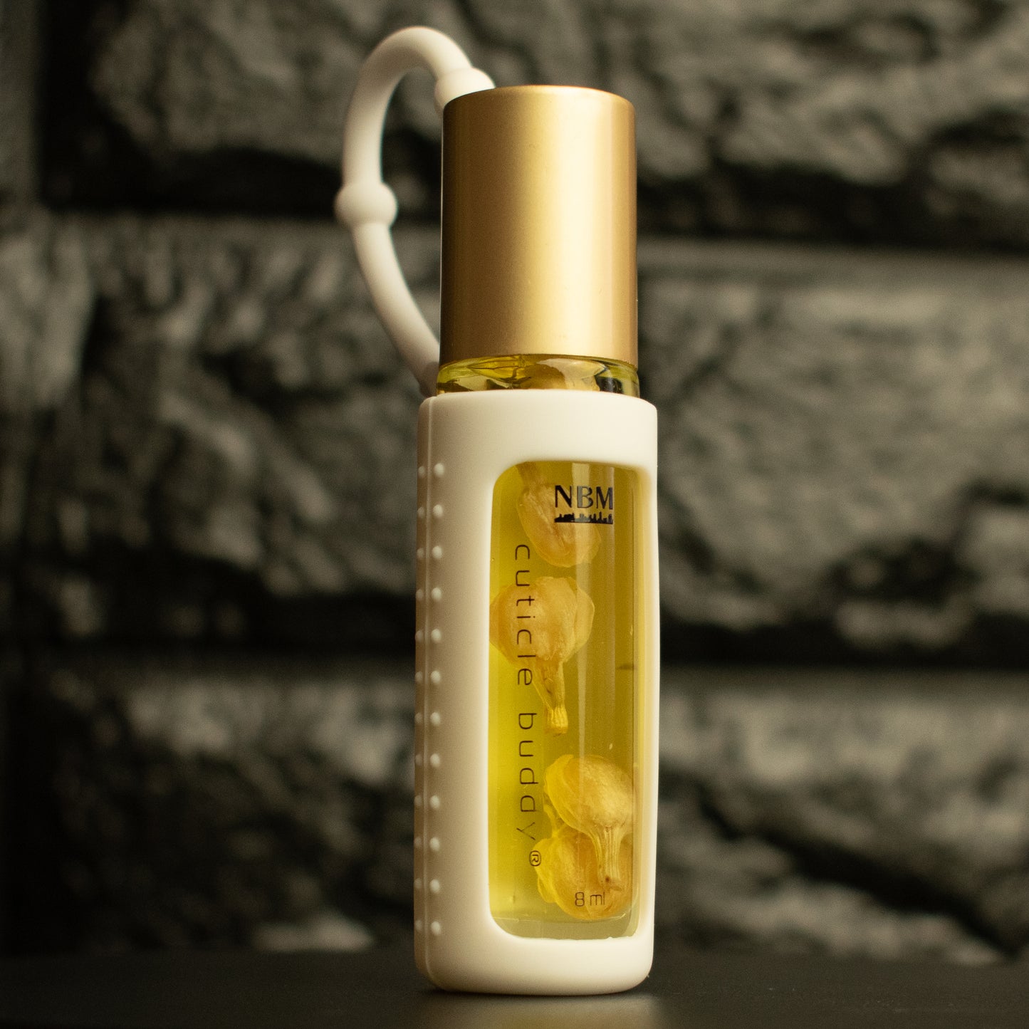 a bottle of cuticle oil with a gold cap, white silicone holder, and jasmine buds inside