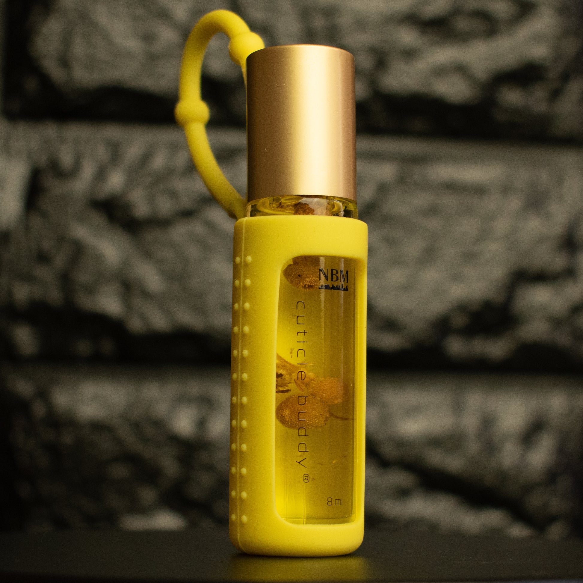 a bottle of cuticle oil with a gold cap in a yellow silicone holder and chamomile buds inside