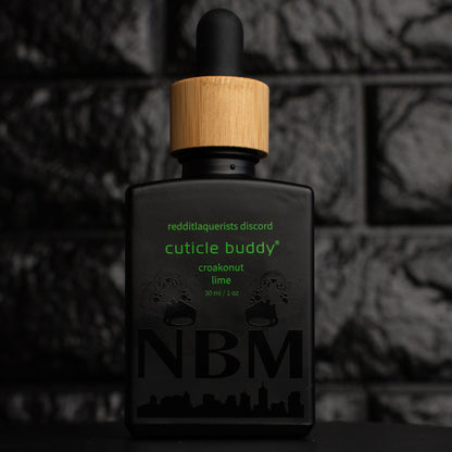a 30ml matte black bottle of coconut lime verbena scented cuticle oil with a bamboo rubber dropper cap and little frog graphics on the bottle