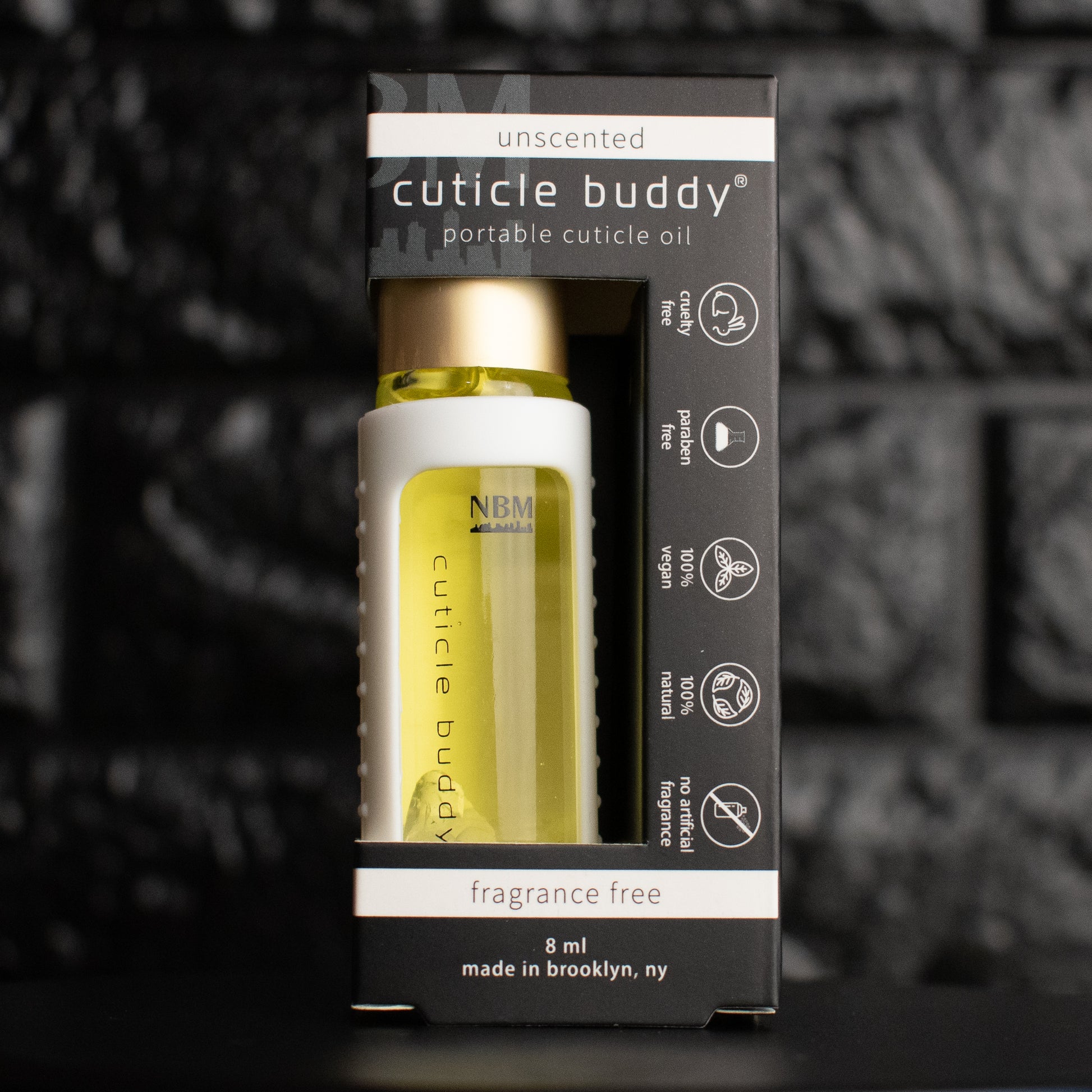 a glass bottle of oil with a gold aluminum cap in a white silicone holder on a black brick background. inside the bottle are clear quartz stones. in its packaging box