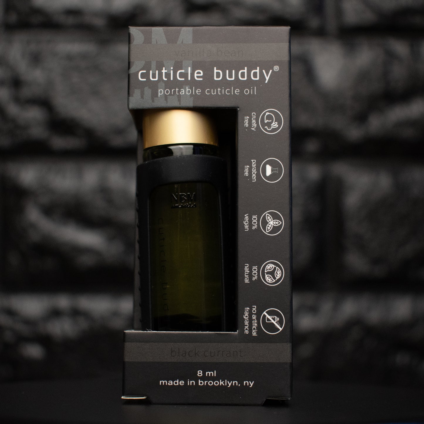 bottle of cuticle oil with gold cap in a black silicone holder in its packaging box
