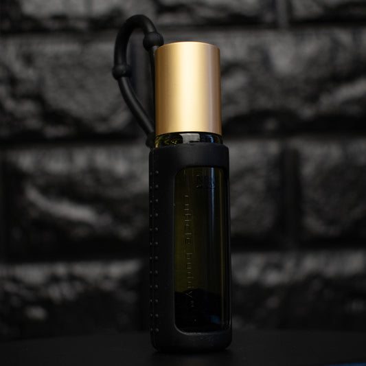a glass bottle of oil with a gold aluminum cap in a black silicone holder on a black brick background. inside the bottle are black obsidian stones