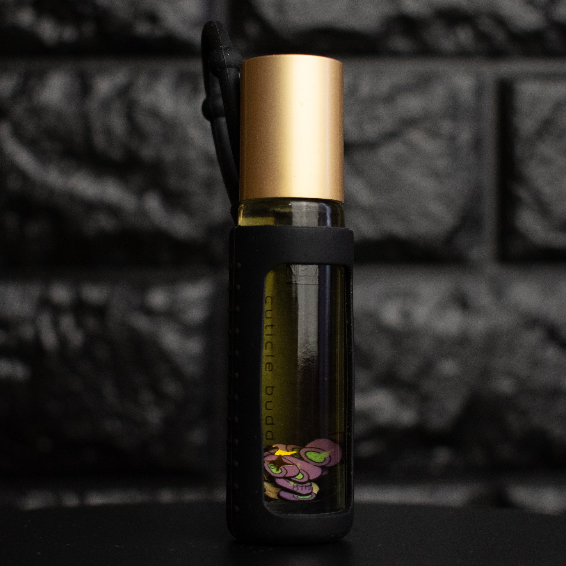 Small glass bottle with gold cap and black label against a dark textured background