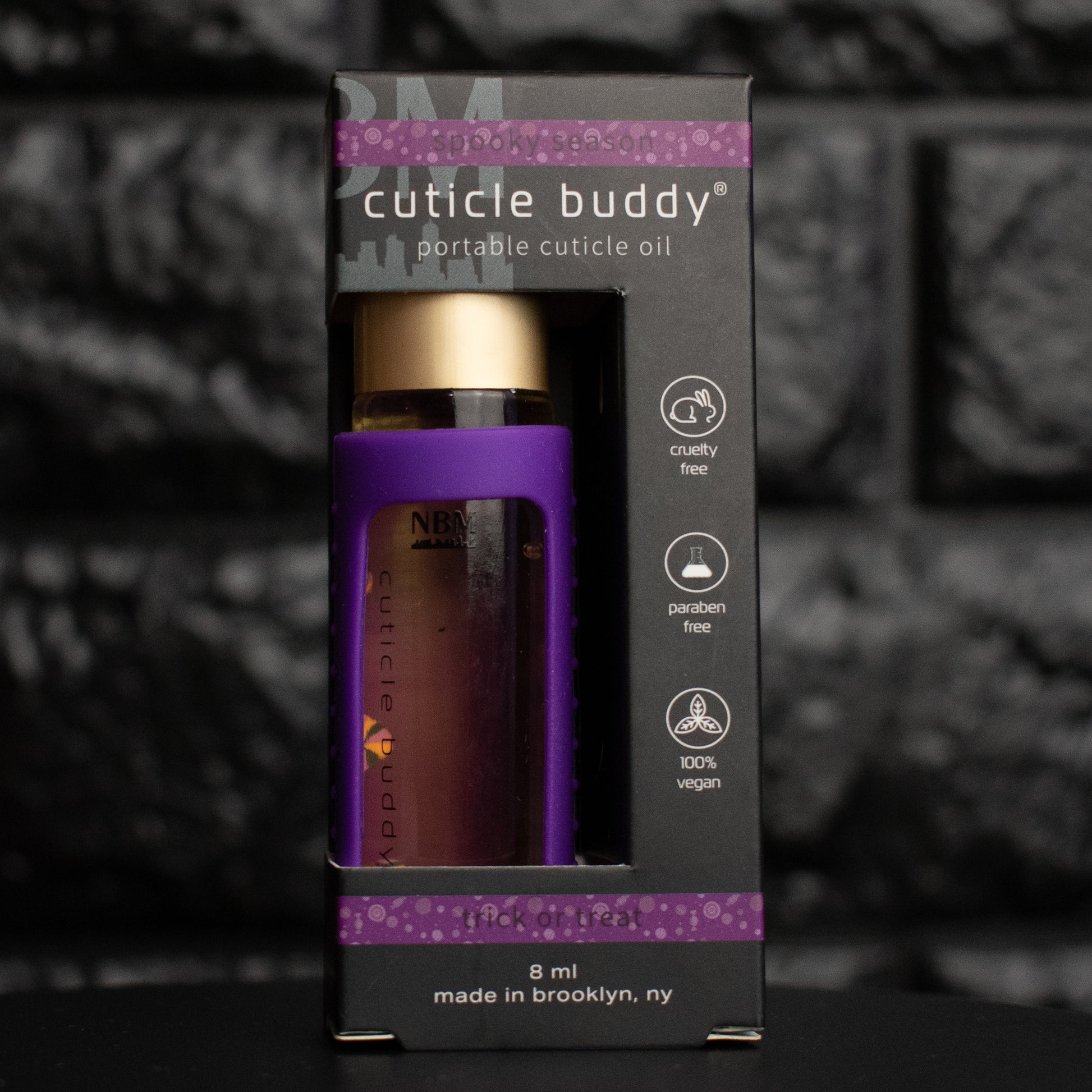 Purple cuticle oil bottle in packaging with 'cuticle buddy' branding on a dark background