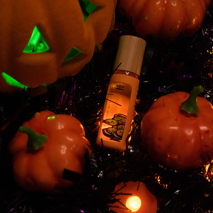 8 ml bottle of cuticle buddy with orange silicone holder and jack-o'-lantern fimo clay slices floating inside displayed amongst pumpkins