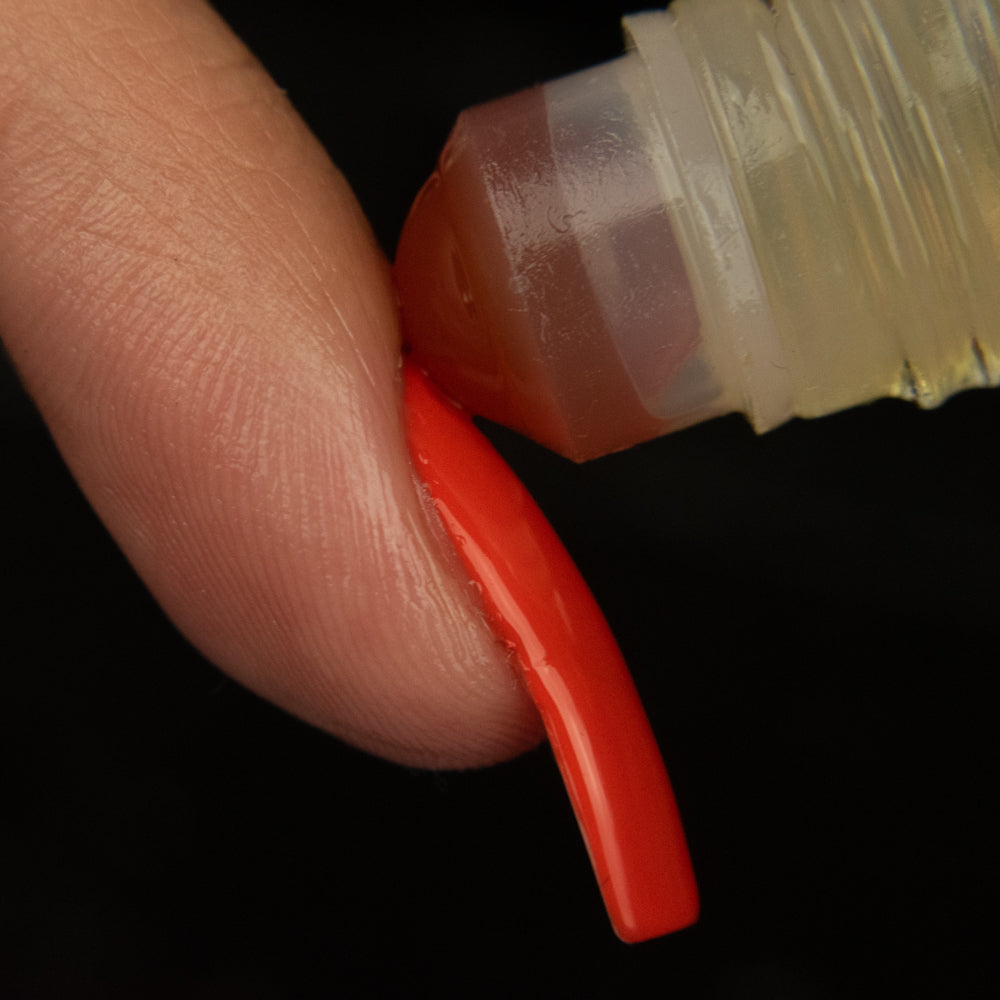 red agate rollerball rolling on the cuticle area of a finger with a long nail painted orange