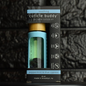 cuticle buddy™ soothing portable cuticle oil inside of it's box in front of black brick