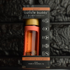 cuticle buddy™ growth portable cuticle oil  inside it's packaging box in front of black brick