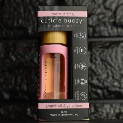 cuticle buddy™ moisturizing portable cuticle oil inside it's packaging box in front of black brick